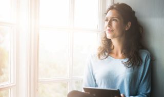 Thoughtful young woman holding digital tablet by window