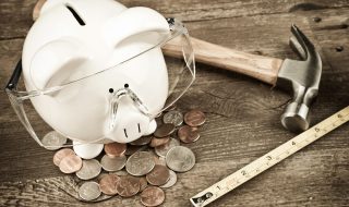 Piggy bank wearing safety goggles with hammer and tape measure on old wood background.