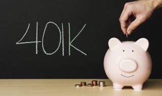 Piggybank on wooden table with stacks of coins beside it. A hand putting a coin into the piggy bank with
