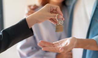Young Asian couple receiving new apartment or room key from realtor or real estate sales agent after finish a rental or buying contract.